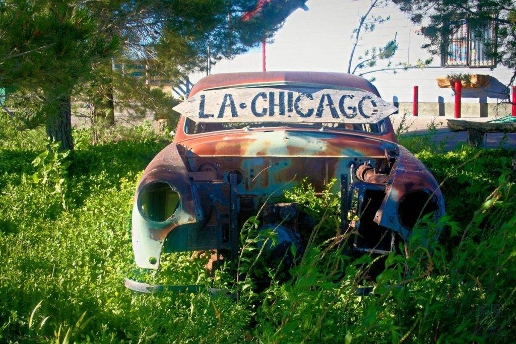 Old rusty car that says LA to Chicago on back. Sitting in a field with grass growing around it