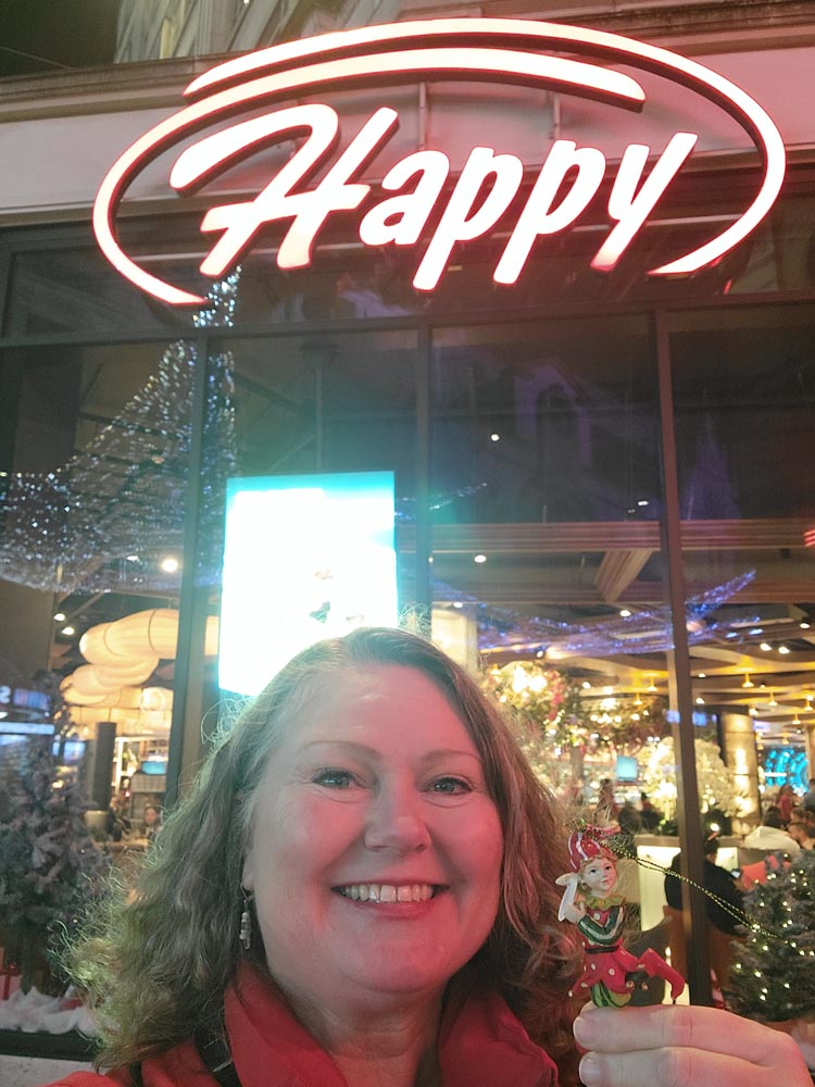 Theresa in London with a neon sign saying Happy above her head.